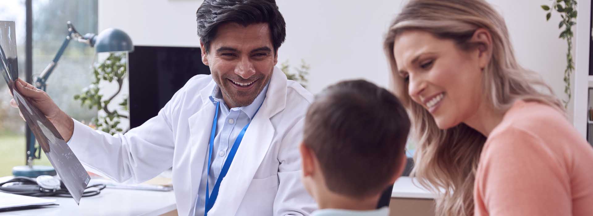 Doctor Or GP In White Coat Meeting Mother And Son For Appointment In Office